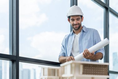 Akıllı inşaat mühendisi ev modeli ve mimari ekipmanlara bakarken ayakta duruyor, yürüyor. Kasklı bir mühendis bina modelinin yanında dururken şehir manzarası yakınında duruyor. İzleme.