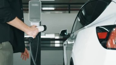 Genç adam EV elektrikli arabasıyla şehir merkezindeki alışveriş merkezinin otoparkına gidiyor şehir merkezindeki sürdürülebilirlik yaşam tarzını yeşil, temiz, yeniden şarj edilebilir elektrikli araç iç organlarıyla şarj ediyor.