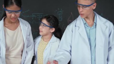 Zeki çocuk deney yaparken deney kabında sıvı karıştırıyor. Akademik öğrenci laboratuvar önlüğü giyerken masada mikroskop ve deneysel ekipmanlarla renkli örnekler koyuyor. Öğretim