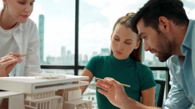 Beyaz proje yöneticisi dizüstü bilgisayar analiz verilerini kullanırken, mimar mühendis ekibi ev modeli inşaatını analiz etmek için birlikte çalışıyor. Bir grup tasarımcı ev tasarımı hakkında konuşuyor. İzleme