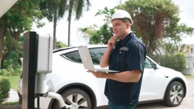 Evde EV şarj istasyonu kurulumu üzerinde çalışan nitelikli teknisyen, EV için dizüstü bilgisayarla şarj sisteminde sorun çıkarma ve yapılandırma ayarları yapıyor. Titiz