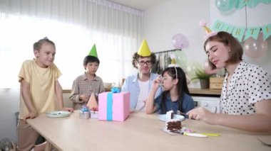 Çekici aile, modern mutfakta masaya konmuş renkli balonla süslenmiş bir şekilde konuşurken kızının doğum gününü kutluyor. Mutlu Asyalı kız gülümseyen ailesiyle pasta yiyor. Pedagoji.