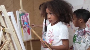 Asyalı çocukla resim yapan ya da tuval çizen mutlu Afrikalı kız. Bir grup oyuncu öğrenci suluboya resim ya da resim yapıyor. Yaratıcılık aktivite konsepti. Etkinlik.