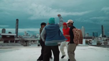 Çok kültürlü veya çok kültürlü hipster grupları şık ve renkli giysiler giyerek çatıda şehir manzaralı ve gökyüzü kazıyıcılarıyla dans ederler. Canlı sokak dansı konsepti. Açık hava sporu 2024 hiphop..