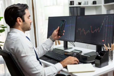 Akıllı telefondan akıllı telefon arayan tüccar işadamı, bilgisayardaki dinamik borsa yatırım ekranını analiz ediyor ve modern merkez ofisteki en kârlı finansal teknoloji pazarına yatırım yapıyor. Tahmin et..