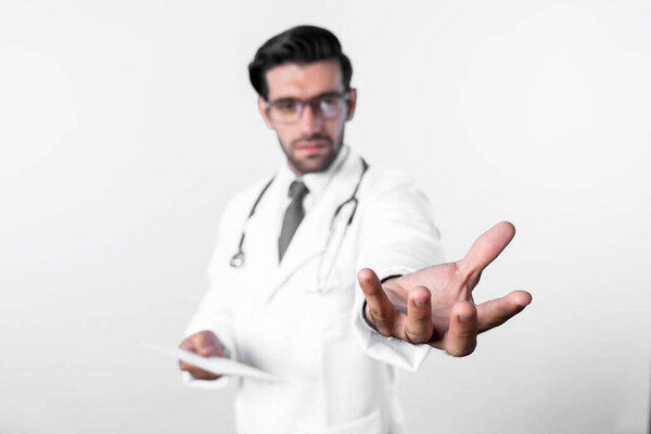 Close up of skilled doctor holding something his hands while standing at blue background. Professional smart doctor holding and wearing glasses, lab coat and stethoscope. Medical therapy. Deviation.