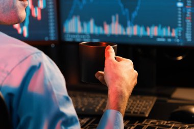 Neon Modern Ofis 'teki bulanık ekranda gerçek zamanlı olarak pazar stoku grafik verilerine odaklanmış kahve fincanı tutan kırpılmış genç tüccar. Finansal değişimi analiz etme kavramı. Toplayıcı.
