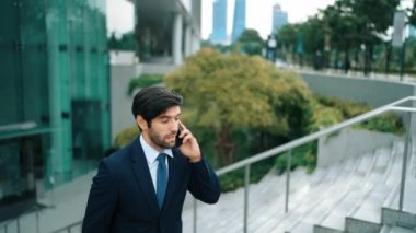 Gülümseyen yakışıklı iş adamı, parkın merdivenlerinde yürürken aynı zamanda işletme müdürünü arıyor. Yatırımcı işe giderken meslektaşıyla konuşuyor. Sevinçli..