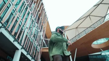 Hip hop tarzında düşük açılı hipster pozu alışveriş merkezi veya bina manzarası ile çevrilidir. Kameraya bakarken Asyalı hip hop koreografı break dans yapıyor. Açık hava sporu 2024 hiphop..