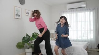 Yatak odasında Asyalı kızıyla müzik eşliğinde dans eden mutlu çekici anne. Beyaz anne dans eder ya da egzersiz yapar. Bu arada tatlı çocuk da müzik eşliğinde yatağa atlar. Aile eğlence konsepti. Pedagoji.