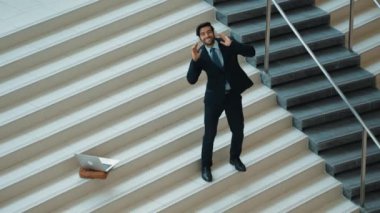Kulaklıktan müzik eşliğinde merdivenlerde duran profesyonel bir iş adamı. Merdivenlere dizüstü bilgisayar yerleştirip dans ederken dinlenme sesi dinleyen yetenekli bir proje yöneticisi. Modern dans. Sevinçli..