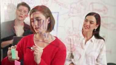 Profesyonel iş adamları pazarlama projesi için beyin fırtınası yapıyor ve birlikte çalışıyorlar. Kafkasyalı kadın lider fikrini nota yazarken iş arkadaşı da fikrini kendine güvenerek sunuyor. Tertemiz..