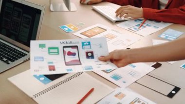 Mobil uygulama için kullanıcı arayüzü prototipini ofis çalışanlarına sunan harika bir şirket çalışanı. UX UI tasarımcısı kağıt üzerinde simge tasarımının işlevini açıklıyor. Sinerjik