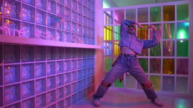 Gece kulübünde kameraya bakarken güneş gözlüklü Asyalı dansçı serbest dans ediyor. Mutlu sokak dansçısı dans ediyor ve renkli parlak neon ışığı ya da yol gösteren ışıkla ayak seslerini gösteriyor. Mutluluk.