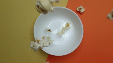 Patlamış mısır, turuncu ve sarı arka planda bir kaseden uçuyor. Beyaz kaseye düşen ve düşen patlamış mısırın yukarıdan görünüşü. Sıradan atıştırmalık konsepti. Poster için tasarım, duvar kağıdı. Pabulum.