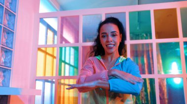 Neşeli İspanyol kız gece kulübünde renkli giysiler giyerken neon ışıkta müzik eşliğinde hareket ediyor. Sokak dansçısı kameraya bakarken hareketli adımlar atıyor. Mutluluk.