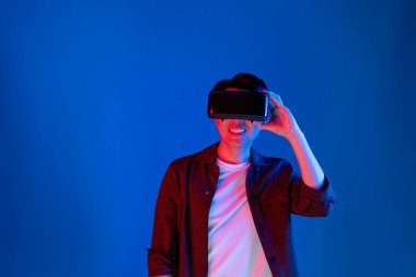 VR 'a bakan Asyalı adam, ilginç nesne teknolojisi üzerine fantastik meta-meta izlemeyi seviyor. Sanal gerçeklik üzerine mavi neon ışıklandırma arka planı. Üç boyutlu hologram yeniliğinde yeni dünya. Entrika.