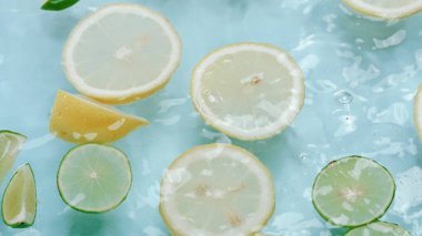 Dilimlenmiş limon makrosu, limon ve limonla suya dökülüyor. Mavi arka planda yüzüyor. Citrus meyve hareketi berrak suda ilerliyor. Citrus tazeliği. Tazelik ve susuzluk kavramı. Pabulum.