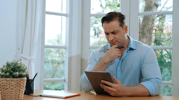 stock image Businessman struggle to solve work problem from home using laptop, sitting on his desk at home office with stressed and frustrated expression, trying to figure out solution for problem. Synchronos