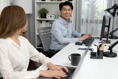 Gülümseyen Asyalı bir adam, yan görüntüdeki modern ofis çalışma masasında veri tabanını ararken günlük dizüstü bilgisayarla pazarlama raporu projesini planlarken kadın meslektaşıyla konuşuyor. İnfobahn.