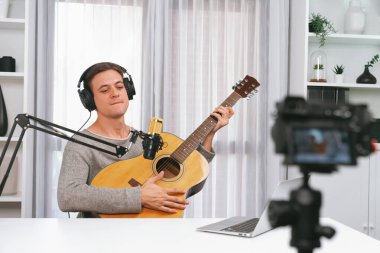 Akıllı şarkıcının sunucu kanalı kamerayla kaydediliyor, gitar çalıyor, sosyal medya kanalından yayın yapıyor, kulaklık takıyor ve beyaz modern stüdyoda video kaydediyor. Bireysel.