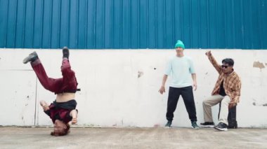 Genç Asyalı dansçı hip hop tarzında dans ediyor ve çok kültürlü arkadaşları duvarın arkasında tezahürat yapıyor. Çekici yakışıklı adam mavi arka planda kollarını uzatıyor. Açık hava sporu 2024 hiphop..
