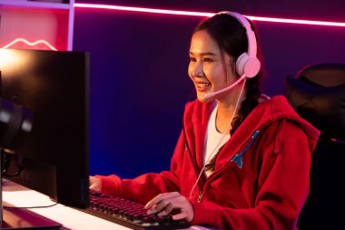 İnternet üzerinden kulaklık takıp gülümseyen Asyalı güzel kız flamasının sunucu kanalı izleyicilerle internet üzerinden konuşma yapıyor. Esport yetenekli takım oyuncuları neon mavi odada. Taktik.