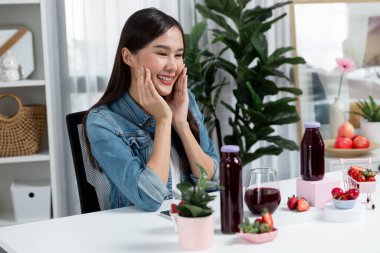 Gülümseyen, güzel Asyalı genç, lezzetli karışık çilek ve kiraz suyu detoksu içeceklerini inceleyen, sosyal medyada özel promosyon satışı için sağlıklı ürünler sergileyen. Taktik.