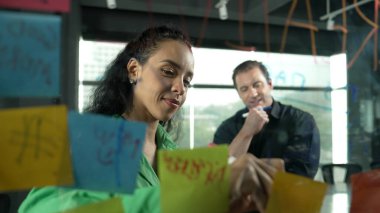 Profesyonel iş adamları yaratıcı pazarlama fikrini modern ofiste tartışırlar. İş adamları cam tahtada yapışkan notlar kullanarak finansal plan üzerinde çalışıyor. Yönlendirici.