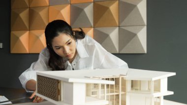 Ev modeli uzunluğunu ölçen Asyalı kadın mimar mühendisinin yakın çekimi. Genç, güzel proje yöneticisi ev modeli üzerinde çalışırken ev inşaatını kontrol ediyor. Yaratıcı tasarım konsepti. Yönlendirici.