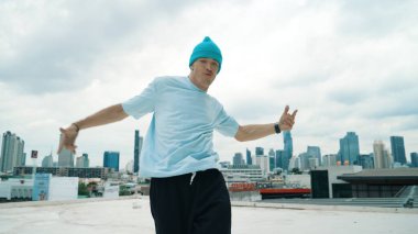 Beyaz dansçı çocuk şehir manzaralı çatıda sokak dansı yapıyor. Hip-hop müziğiyle hareket eden genç adamın sokak dansı sahnesi. Açık hava sporu 2024. ÇalışmaComment.