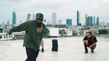 Profesyonel break dans takımı çatıda çok kültürlü arkadaşlar varken break dans alıştırması yapıyor. Genç modern dans grubu hip hop hareketi yapıyor. Tarz, moda, aksiyon. Açık hava sporu 2024. ÇalışmaComment.