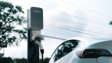 Doğal yeşil şehir parkındaki otoparkta EV elektrikli araba şarj pili. Sürdürülebilir ve çevre dostu şehir yolculuğu için yenilenebilir otomobil için alternatif temiz enerji teknolojisi. Eşzamanlama