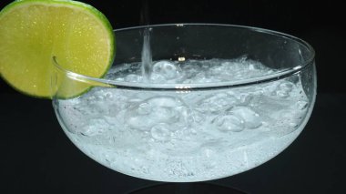 Bir margaritanın makrografisi bir bardağa dolduruluyor canlı bir limon dilimiyle süsleniyor, hepsi siyah arka plana karşı. Her yakın çekim kokteyl ve taze limonun detaylarını yakalar. Geliştirilebilir.