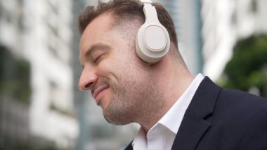 İş adamlarının kulaklıklarını kapat ve neşeli ve motive edici bir şekilde müzik eşliğinde dans et. Yetenekli proje yöneticisi şehir merkezinde bulanık arkaplanlı rahat şarkılar dinlemeyi sever. Urbane.