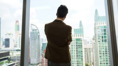 Arkaya bakan hırslı işadamı süslü bir ofiste dikilip şehir manzarası siluetine bakıyor. Kararlılık ve iş hırsı iş kariyerini parlak bir geleceğe taşıdı