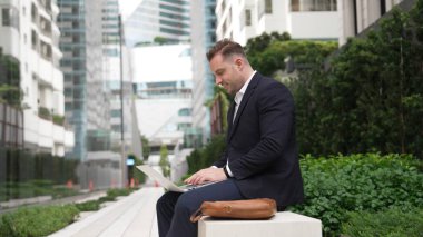 Yeşil Şehir 'deki akıllı proje yöneticisine rapor yazmak için dizüstü bilgisayarı üzerinde çalışıyor. İş adamı analiz verilerine ve beyin fırtınası fikrine bankta otururken bilgisayar kullanarak bakıyor. Urbane.