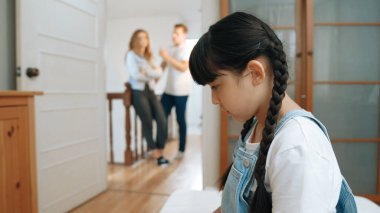 Stresli ve mutsuz genç kız köşeye kıvrılıp kulaklarını kapatarak arka planda ebeveyninin tartışmasını engelliyor. Evde aile içi şiddet ve travmatik çocukluk depresyona dönüşür. Eşzamanlama