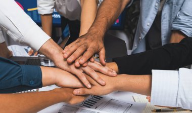 Çeşitli ofis çalışanlarından oluşan bir grup, ofis odasında el ele vererek iş sinerjisini ve iş yerindeki güçlü verimli takım çalışmasını sembolize ediyor. İş çalışanları arasındaki işbirliği ve birlik. Tedbirli