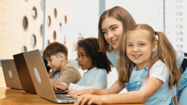 Çok kültürlü bir öğrenci dizüstü bilgisayar kullanarak mühendislik kodları yazarken öğretmen program hakkında açıklama ve öğretim yapıyor. Profesyonel eğitmen BTMM sınıfında programlama sistemini öğrenmeye yardım ediyor. Etkinlik.