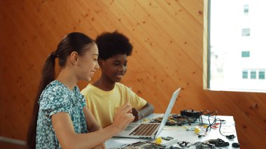 Afrika 'lı bir erkek ve beyaz bir kızın günlük giysiler içinde BTMM teknoloji sınıfında dizüstü bilgisayar ve elektronik ekipmanlarla kod yazma ya da programlama sisteminde birlikte çalıştıklarını gösteren site görüntüsü. Öğretim.