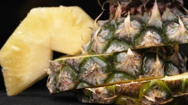 Taze ananaslı ve ayrı siyah arkaplanlı bir ananas dilimli videoyu kapat. Kaba ve balmumu kabuğu, dikenli yeşil yapraklardan bir taç, yemek fotoğrafçılığı. Geliştirilebilir.