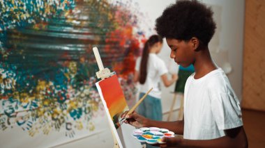 Afrikalı erkek tuvali sıcak tonda boyarken, beyaz elbiseli kız renkli duvarın arkasında havalı renkler çiziyor. Yaratıcı aktivite konsepti. Öğretim.