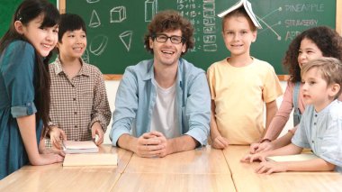 Profesyonel Kafkas öğretmeni ve çeşitli öğrenciler kameraya bakarken mutlu çocuk başparmak gösteriyor. Sınıfın önünde dururken gülümseyen bir grup çok kültürlü çocuk. Eğitim. Pedagoji.