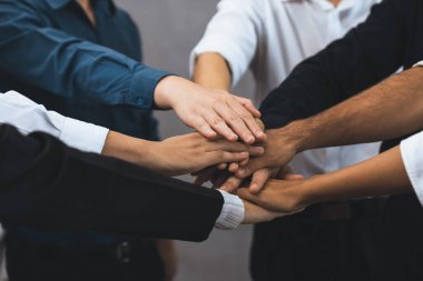 Çeşitli ofis çalışanlarından oluşan bir grup, ofis odasında el ele vererek iş sinerjisini ve iş yerindeki güçlü verimli takım çalışmasını sembolize ediyor. İş çalışanları arasındaki işbirliği ve birlik. Tedbirli