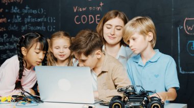 Çocuğun dizüstü bilgisayar mühendisliği kodunu ve yazım programını kullanırken STEM teknoloji sınıfında kontrol sahibi olan çeşitli çocuklardan oluşan bir grubun hemen karatahtayla yazılmış hali. Etkinlik.
