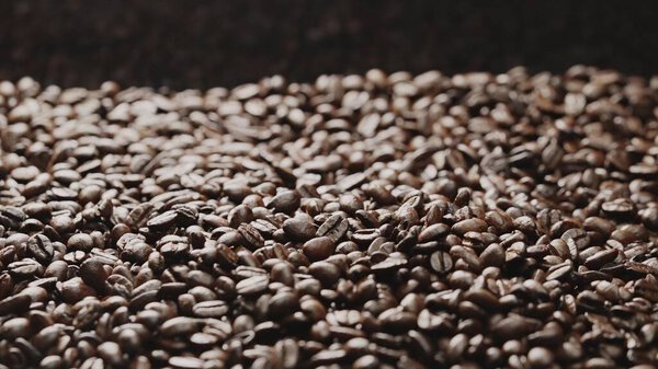 Macro shot of super slow motion shot of fresh coffee bean placed with black background. Close up of piles of aromatic roasted coffee seed surrounded. Macrography. Beans scattering around. Comestible.