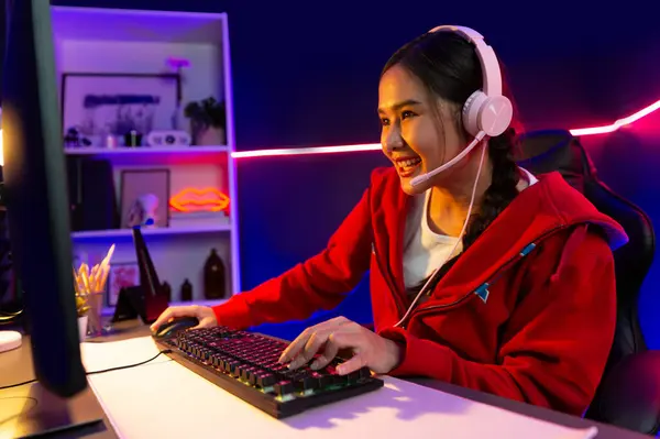 stock image Host channel of smiling beautiful Asian girl streamer playing online game wearing headphone talking with viewers media online recording phone. Esport skilled team players in neon blue room. Stratagem.