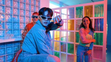 Asyalı adam gece kulübünde çeşitli neon ışıklarda dans ederken kolunu oynatıyor. Modern kulüpte çok kültürlü hippilerle dans eden şık elbiseli mutlu dansçı. Mutluluk.