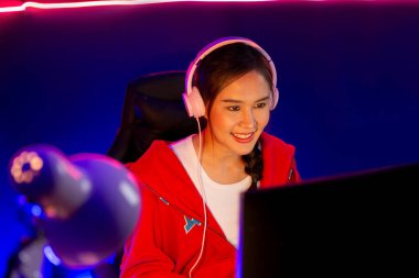 İnternet üzerinden kulaklık takıp gülümseyen Asyalı güzel kız flamasının sunucu kanalı izleyicilerle internet üzerinden konuşma yapıyor. Esport yetenekli takım oyuncuları neon mavi odada. Taktik.